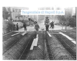 Foto storica in bianco e nero: operai posano l'armatura in ferro dell'impalcato, con betoniera e palazzi sullo sfondo