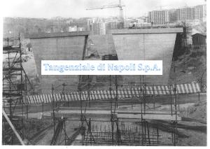 Foto storica: due grandi pile in cemento armato del viadotto in costruzione, ponteggi in primo piano e gru sui palazzi sullo sfondo